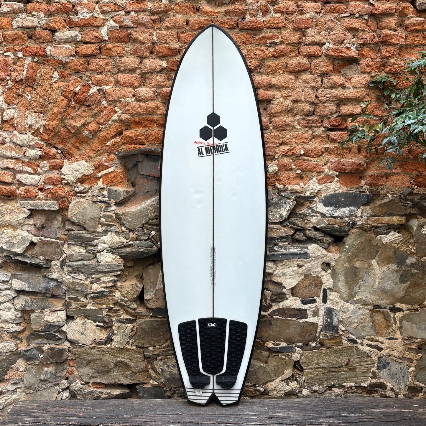 CI Surfboard Bobby Quad leaning against a stone wall with a brick background