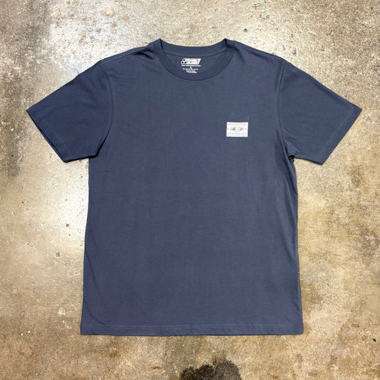 Navy blue Channel Islands t-shirt with a small white logo on a textured beige surface