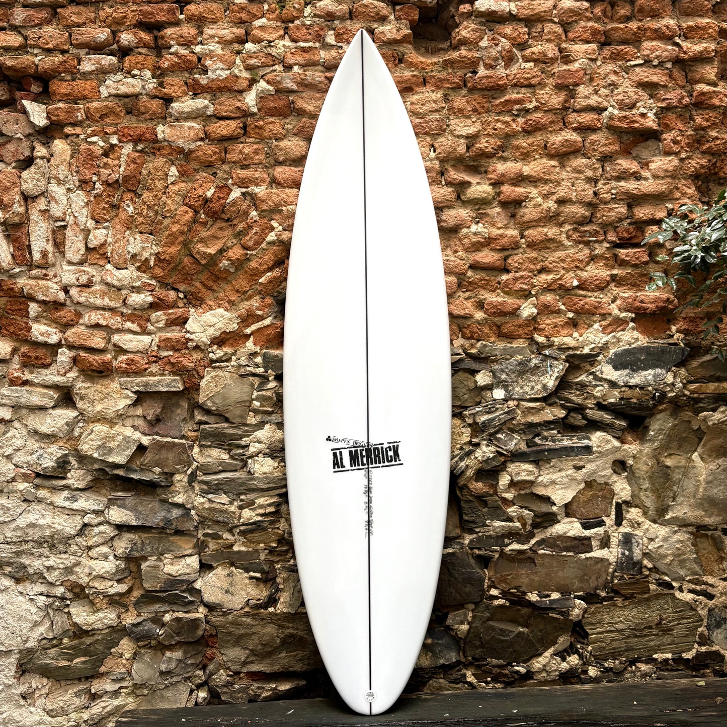 White CHANNEL ISLANDS  CI PRO  STEP UP  6'4x 20 1/8 x 2 3/4  37.3L surfboard with a brand logo against a rustic stone wall.