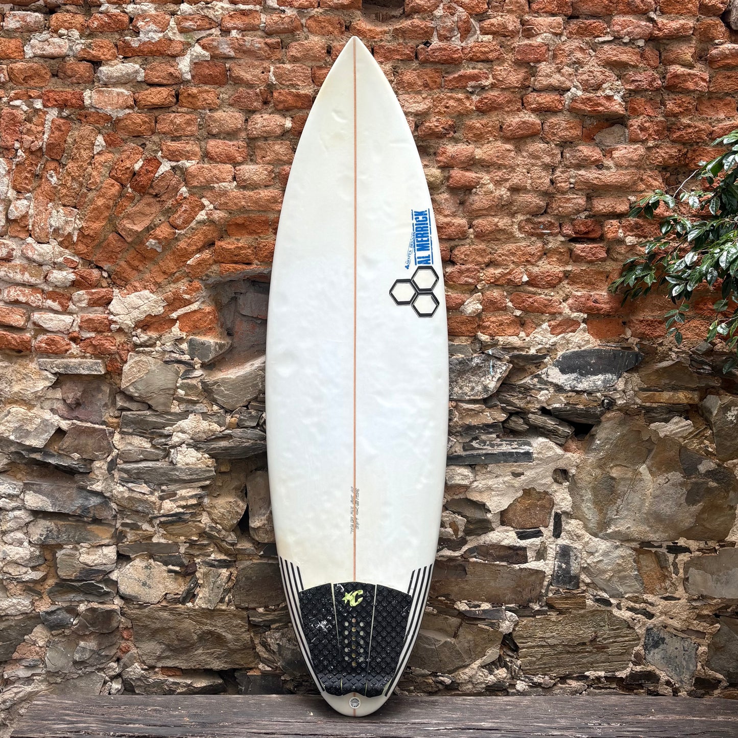 White surfboard with black and blue design leaning against a brick wall.