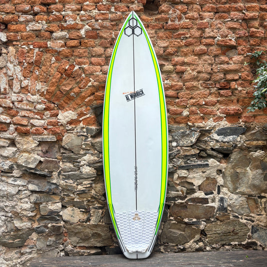 A white surfboard with bright neon green borders and a black center line, leaning against a rustic brick and stone wall.