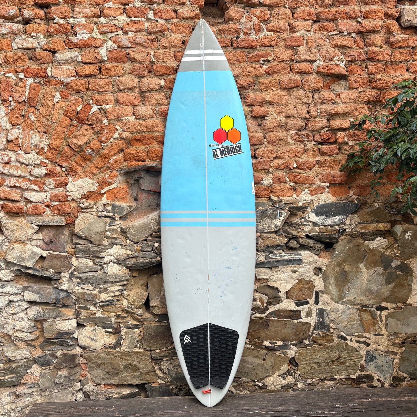 Channel Islands Taco Grinder Surfboard with a colorful design leaning against a stone wall.