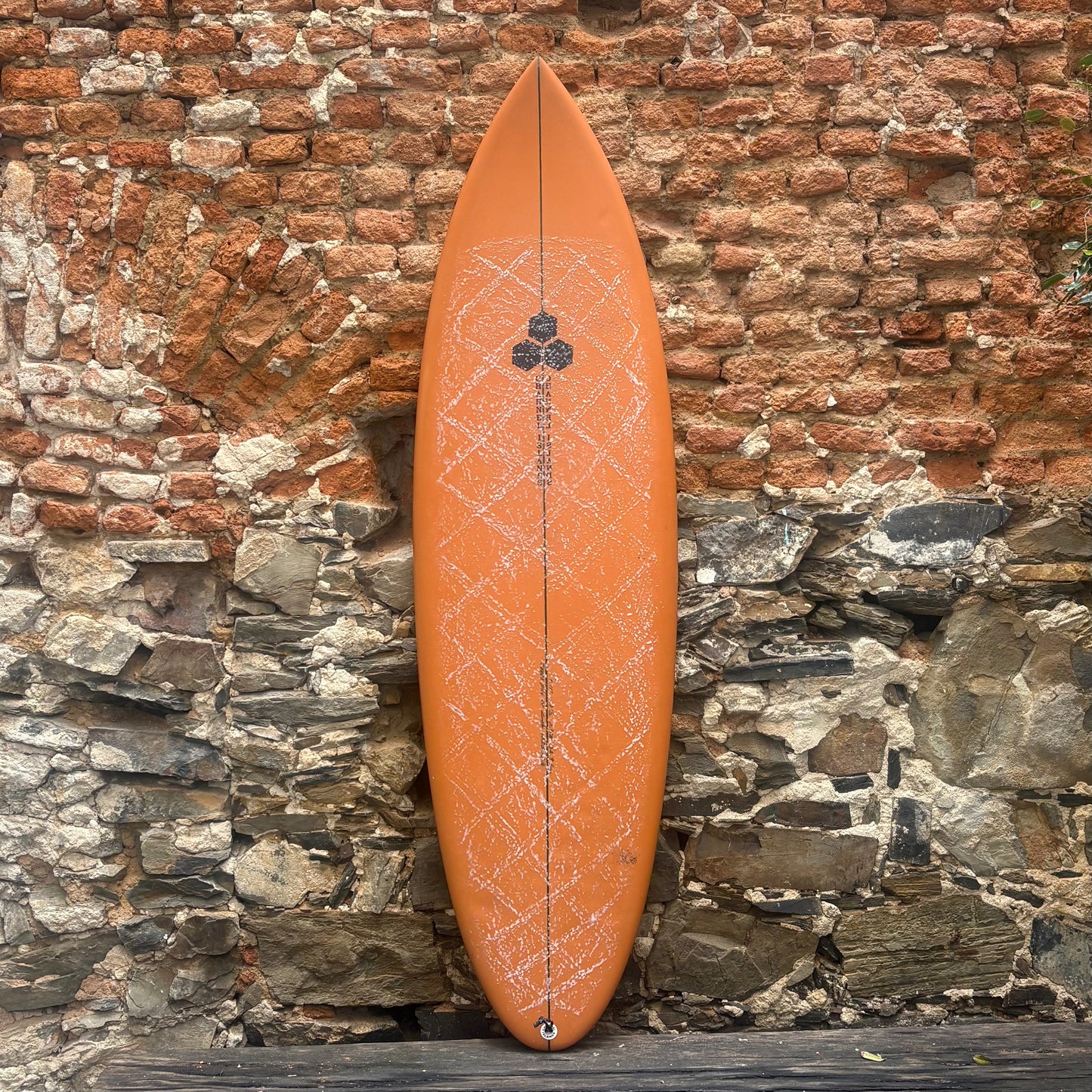Orange surfboard with a geometric pattern leaning against a stone wall.
