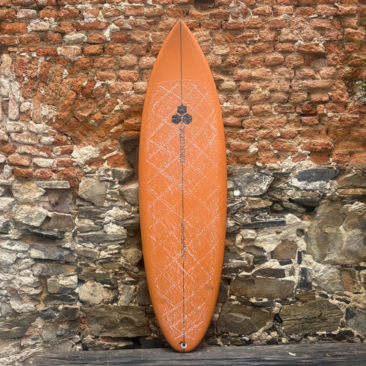 Orange surfboard with a geometric pattern leaning against a stone wall.