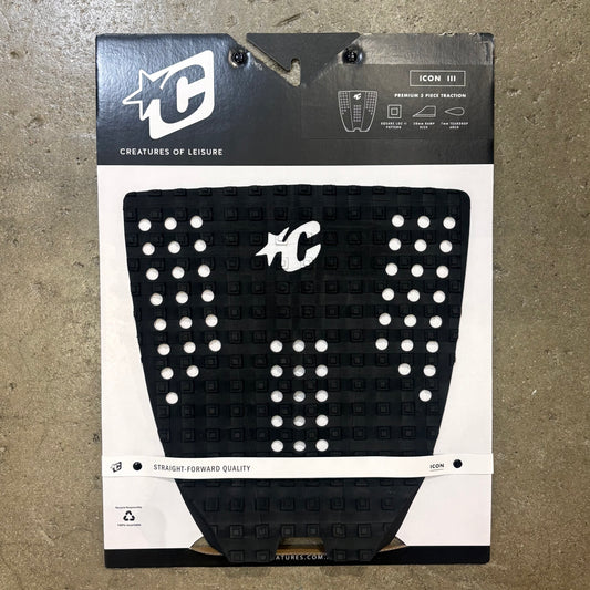 Black and white surfboard tail pad with 'Creatures of Leisure' branding on a textured surface.