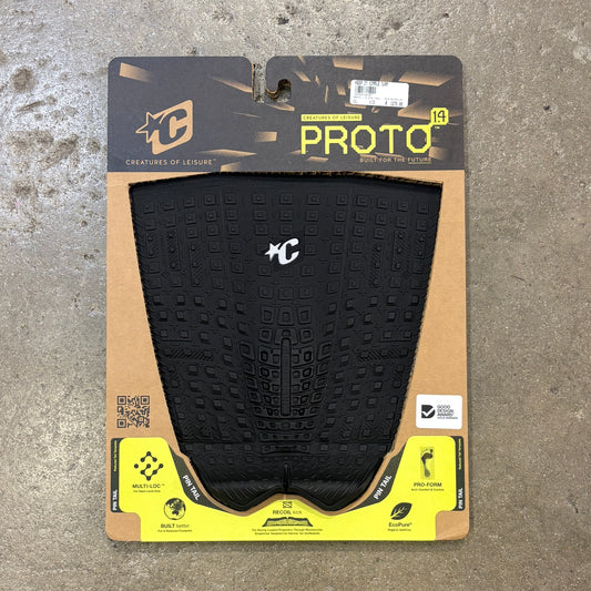 A black Proto 1.5 surfboard deck grip  package by Creatures of Leisure, displayed on a textured gray concrete floor. The grip tape is black with a textured grid pattern and a white 'C' logo, mounted on a cardboard backing with a black and yellow header.