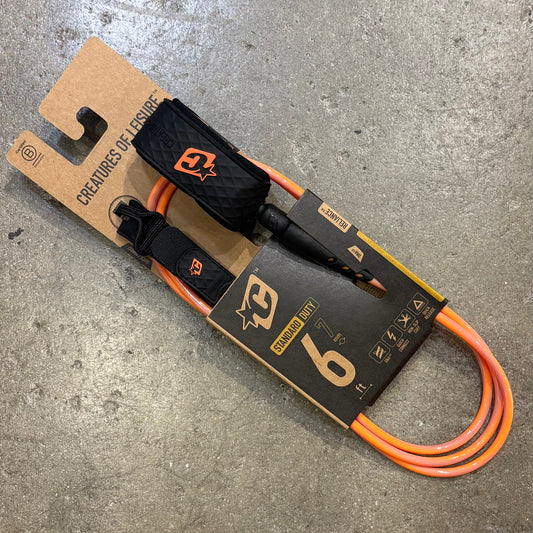 Orange leash with black handle on a 'Creatures of Leisure' branded package on a concrete surface
