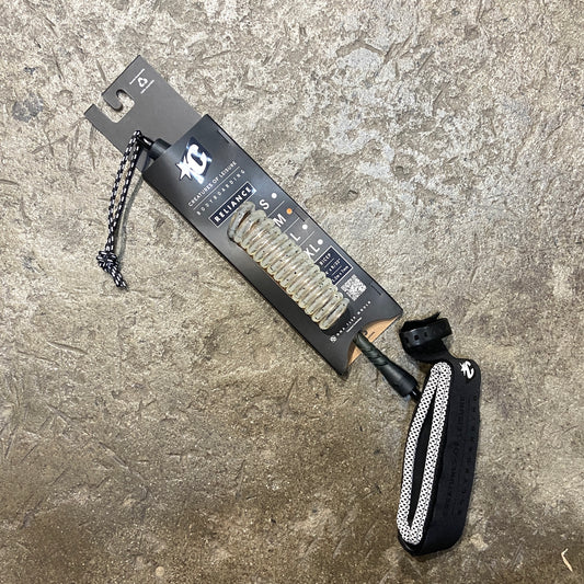 A black bodyboard leash with a non-slip cuff and coiled urethane cord, laid out on a textured surface.