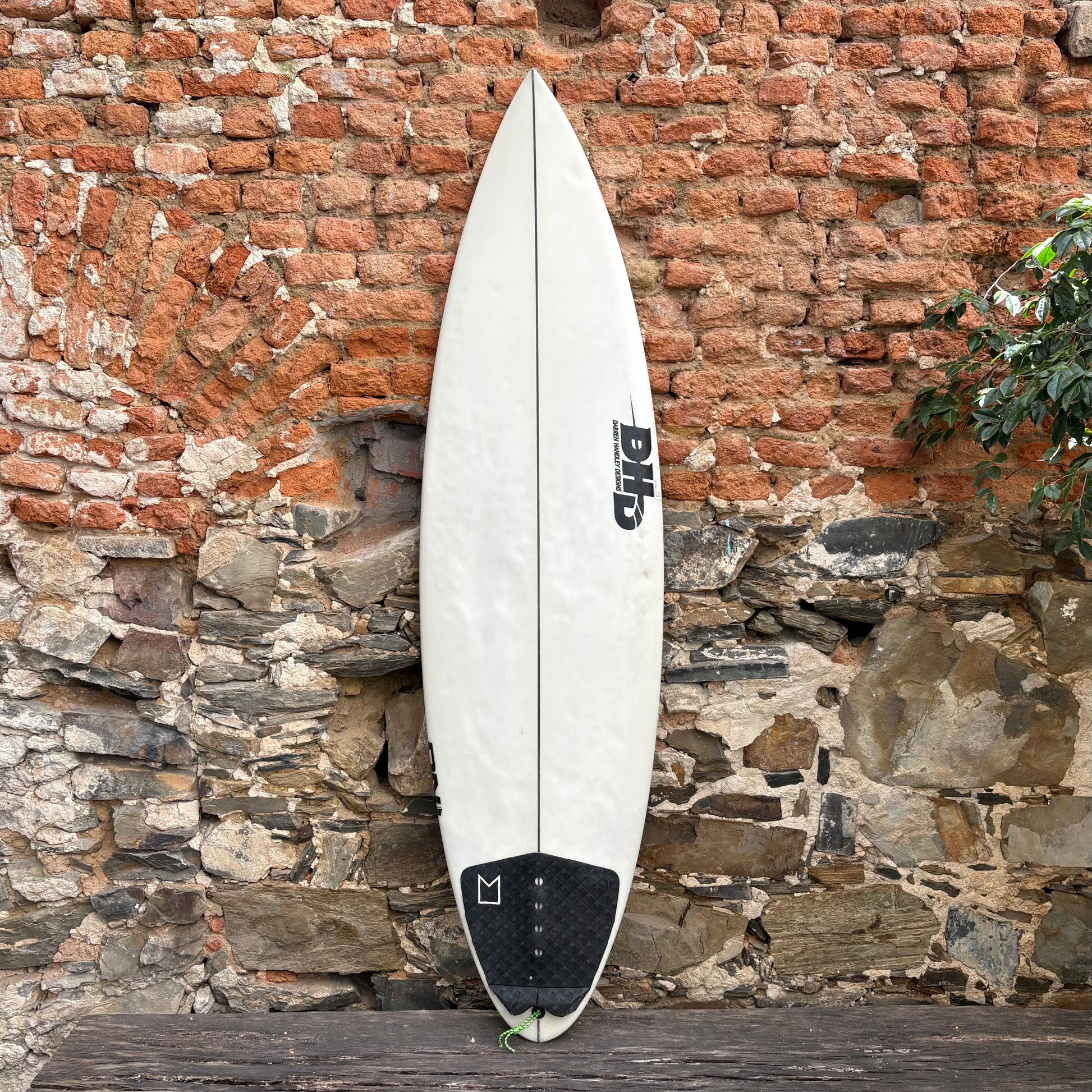 White surfboard with black logo against a rustic stone wall