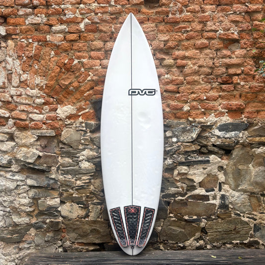 White surfboard with black and red design leaning against a stone wall.