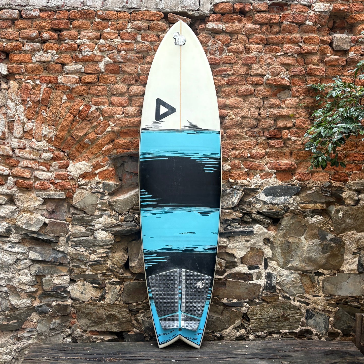 Surfboard with blue and black design leaning against a stone wall.