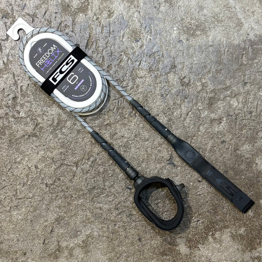 A FCS Freedom Helix Leash - All Round in A clear white colour way lying on a concrete floor 
