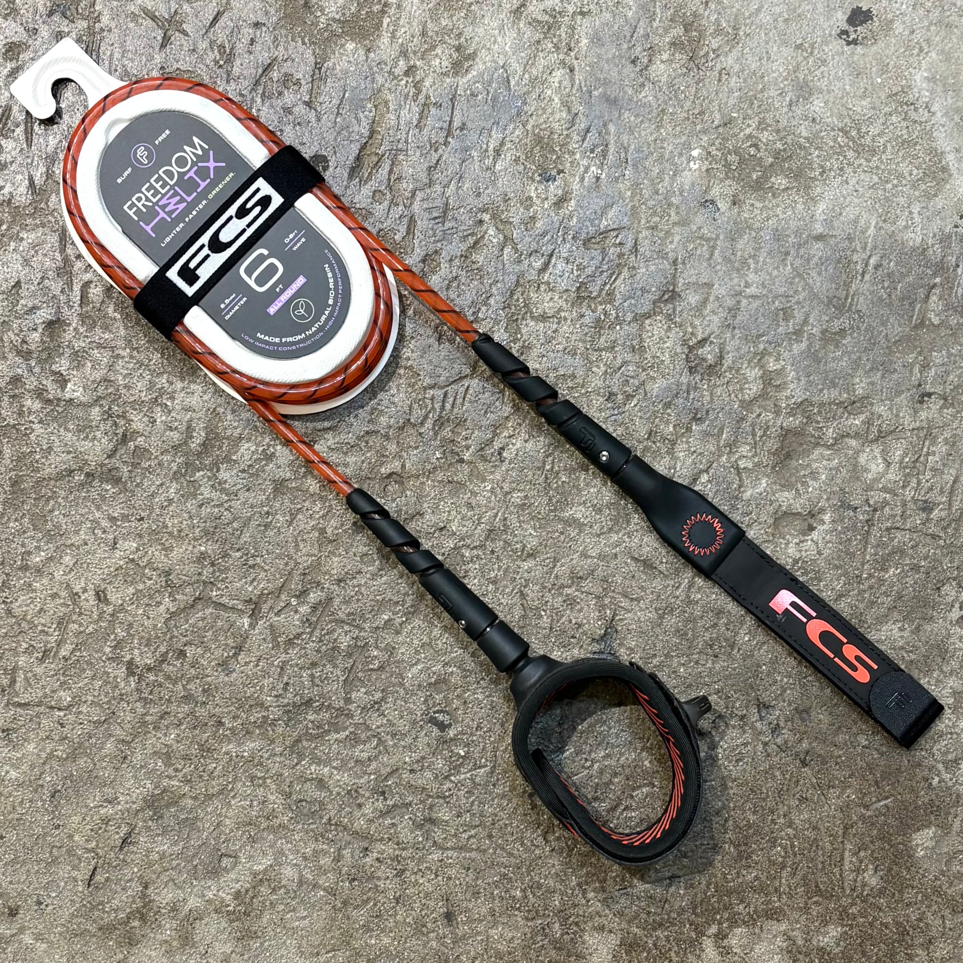 A FCS Freedom Helix Leash - All Round in red lying on a concrete floor 