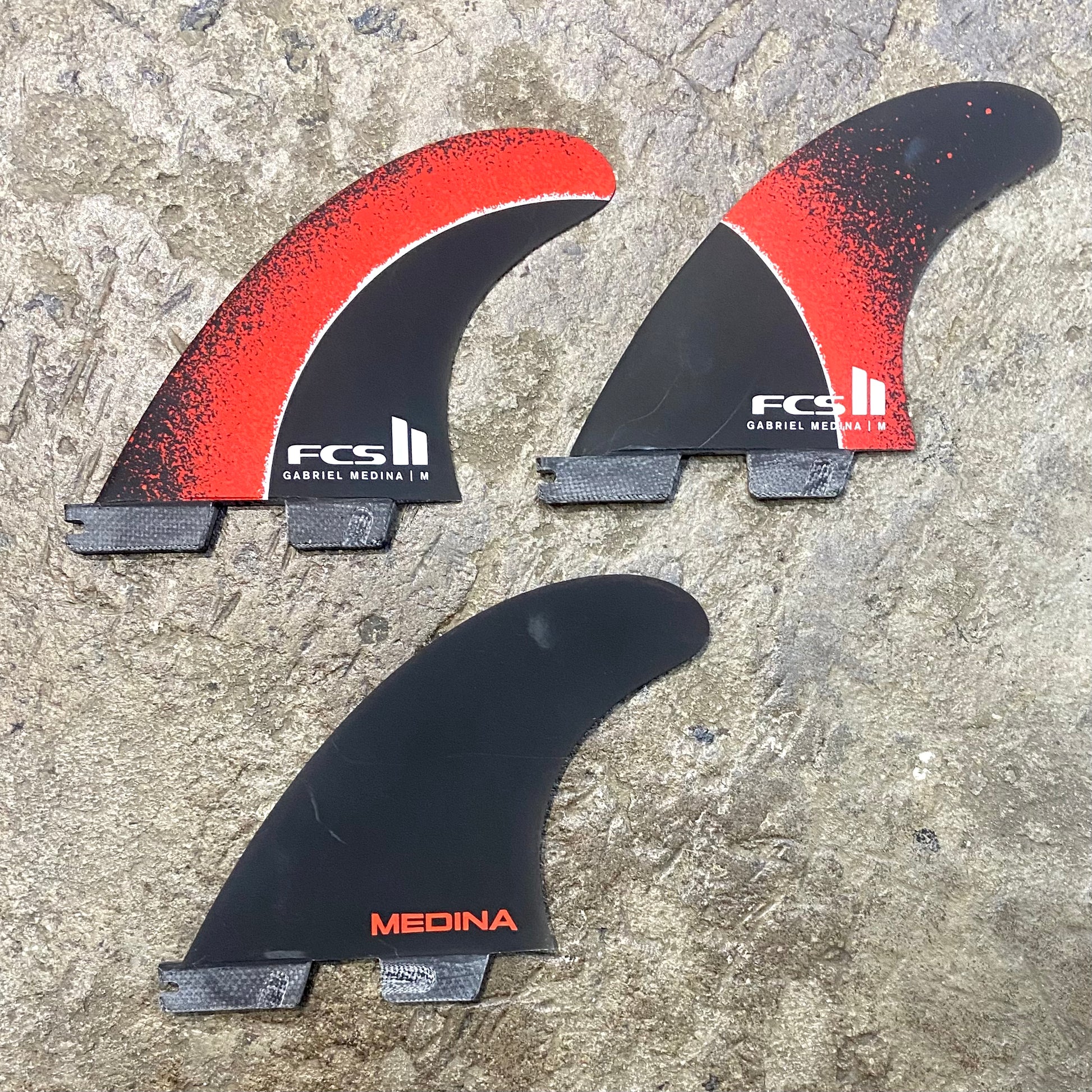 A set of FCS II Gabriel Medina Signature Tri Fins with red, black, and grey color scheme.