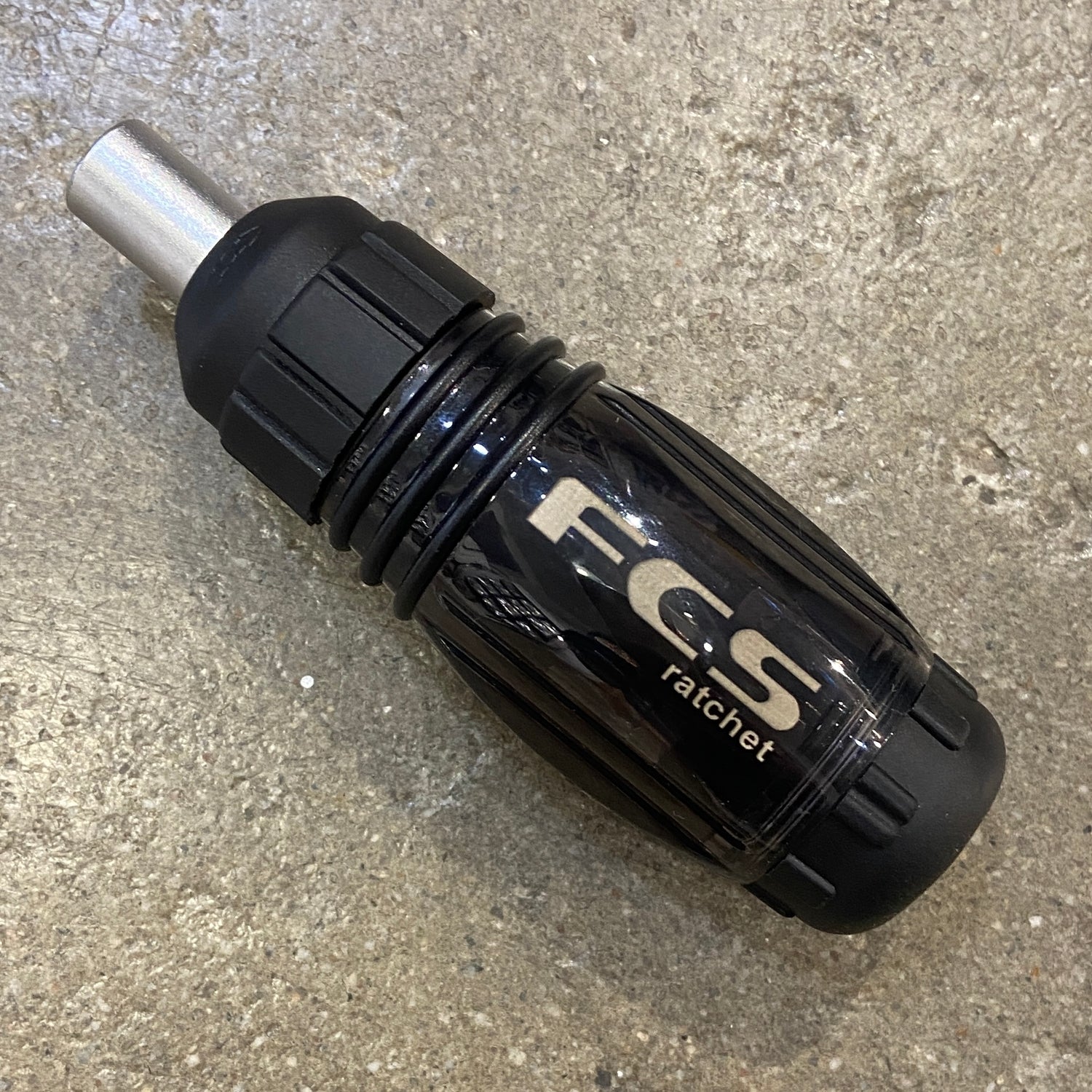 A FCS Ratchet Tool in black laid out on a concrete surface