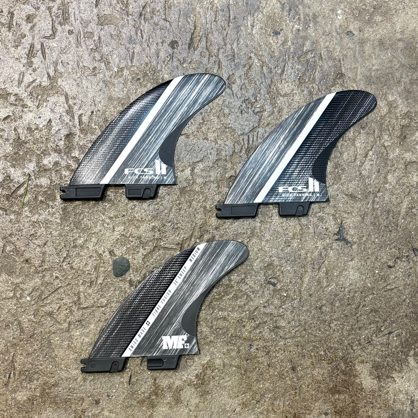 Three carbon fiber surfboard fins with FCS logo on a textured surface