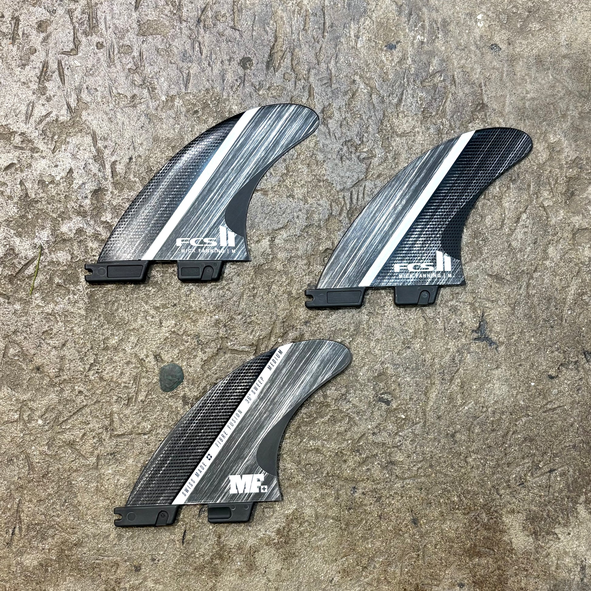 Three carbon fiber surfboard fins with FCS logo on a textured surface