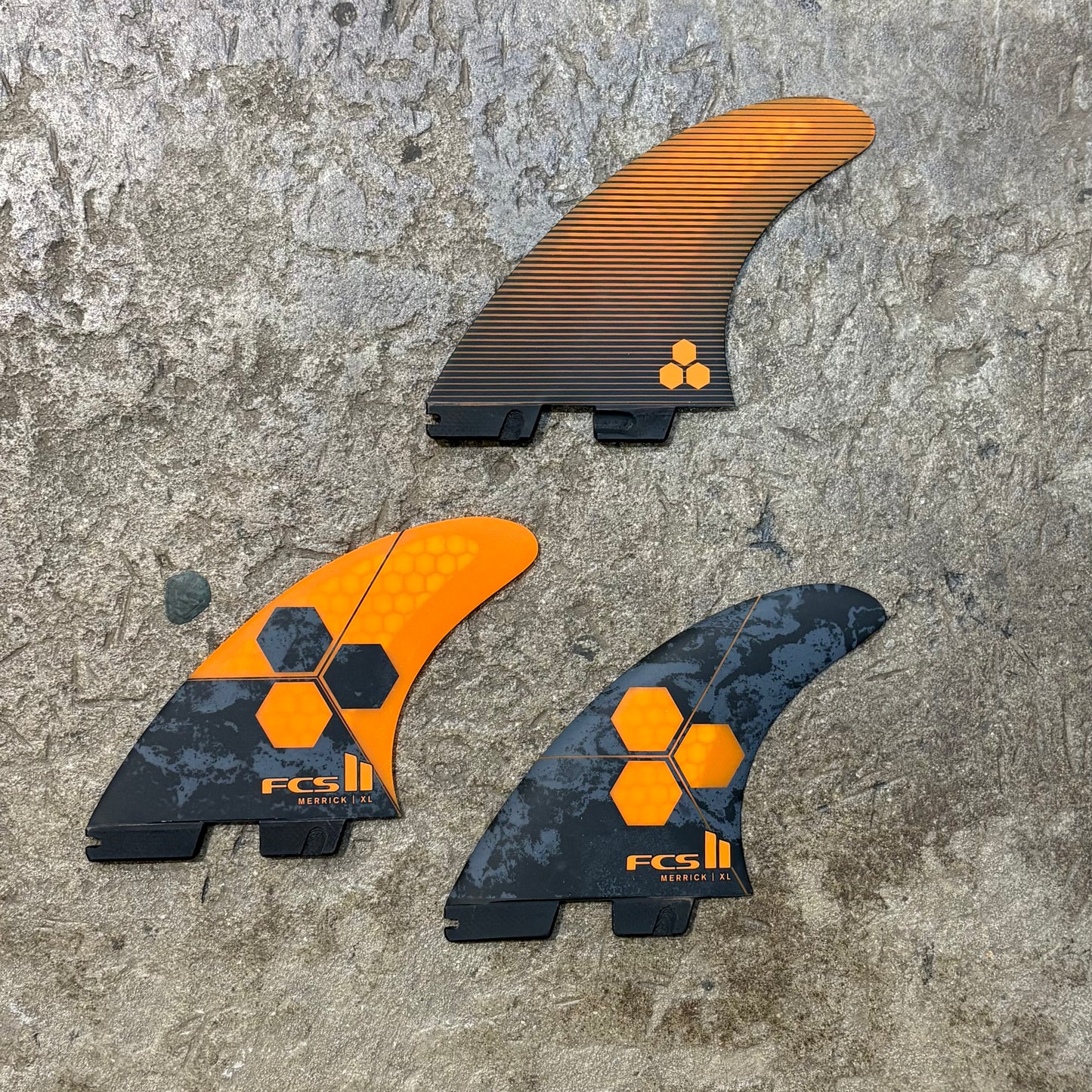 Three FCS surfboard fins on a textured surface