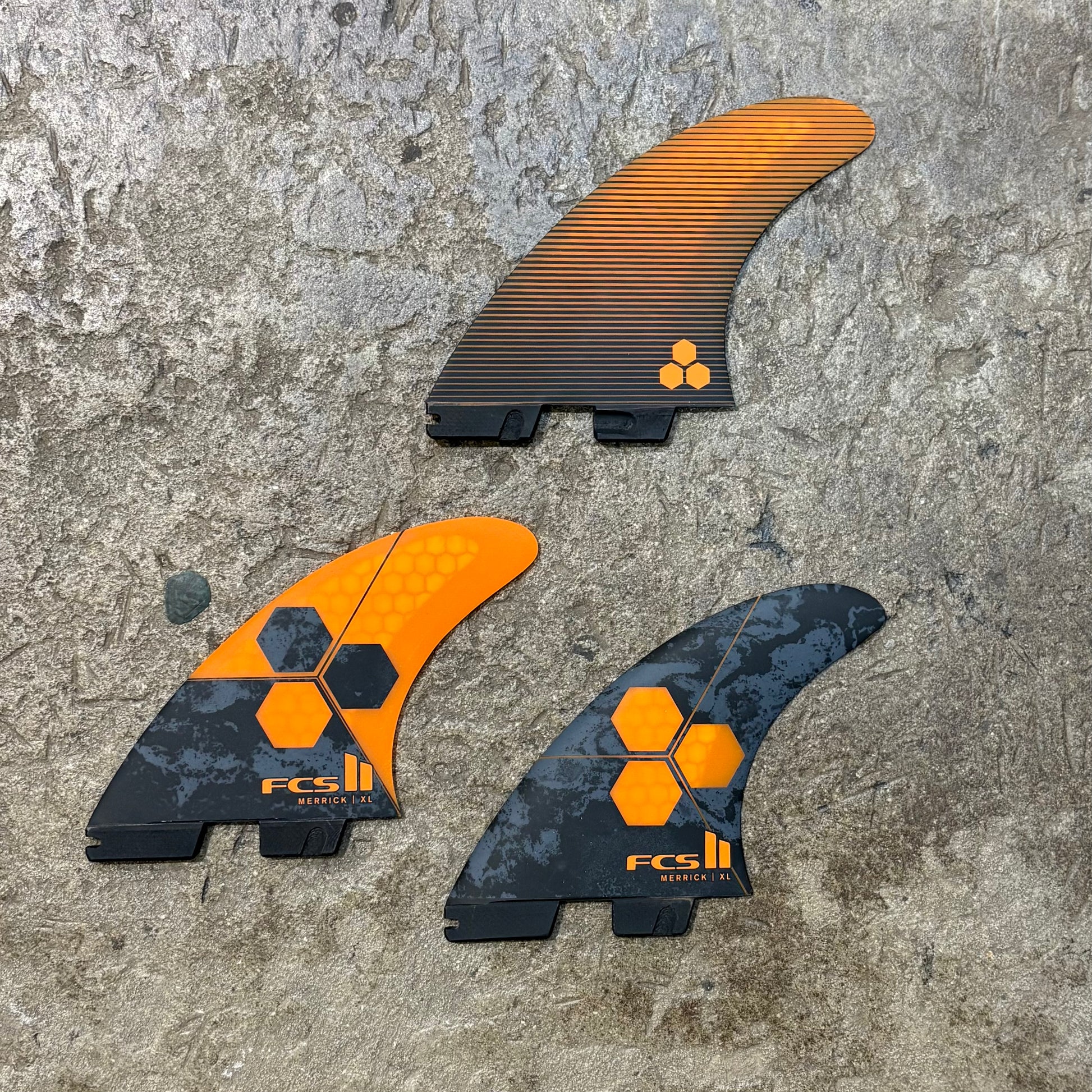 Three FCS surfboard fins on a textured surface