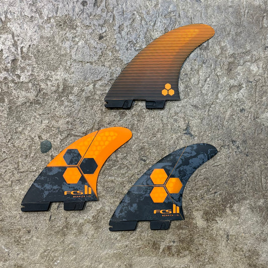 Three FCS surfboard fins on a textured surface