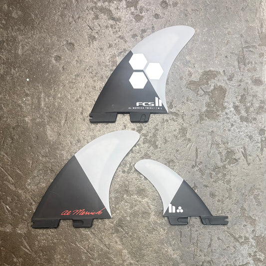 Three surfboard fins with FCS branding on a textured surface