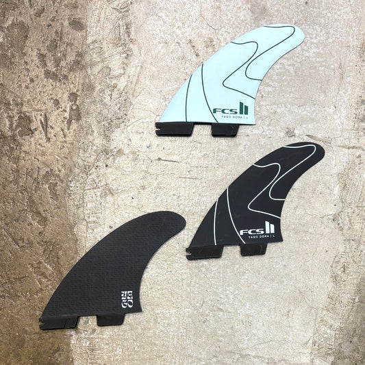 Three surfboard fins with FCS II branding on a textured surface