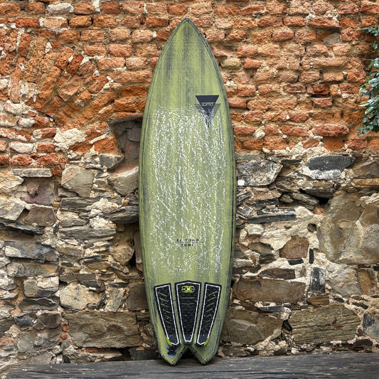 Green Firewire EL TOMO  Surfboard in front of rustic wall.
