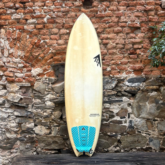 Beige surfboard with blue accent against a rustic stone wall