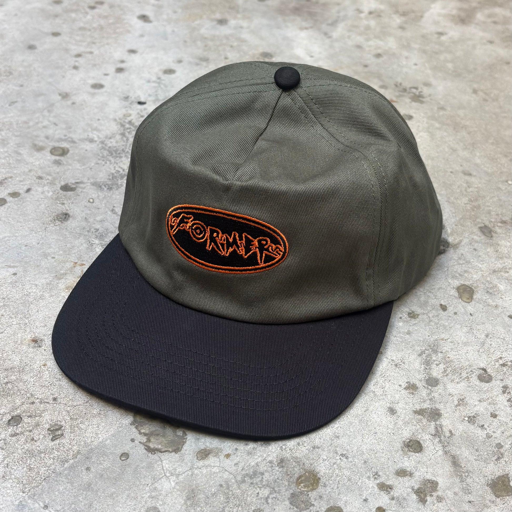 Two-tone cap with orange logo on a concrete surface