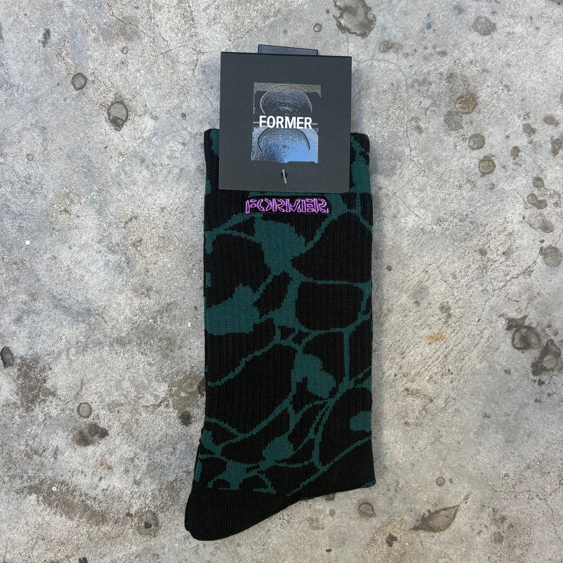 Black and green patterned socks with 'Former' branding on a concrete surface