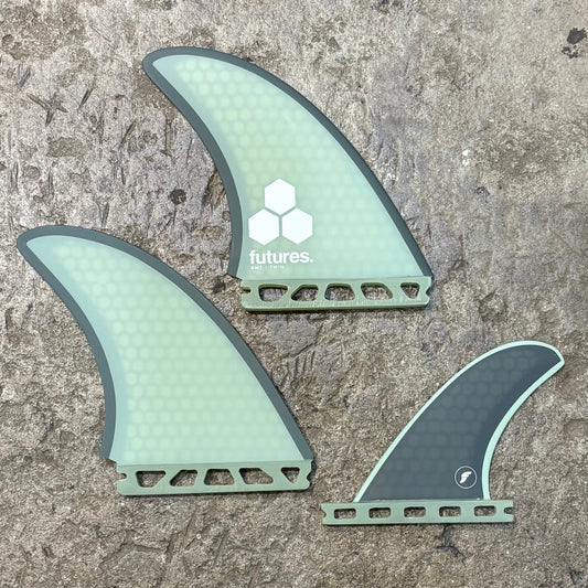 A set of green Futures Al Merrick Twin+1 surfboard fins with the 'futures' and 'Al Merrick' logos on a textured background.