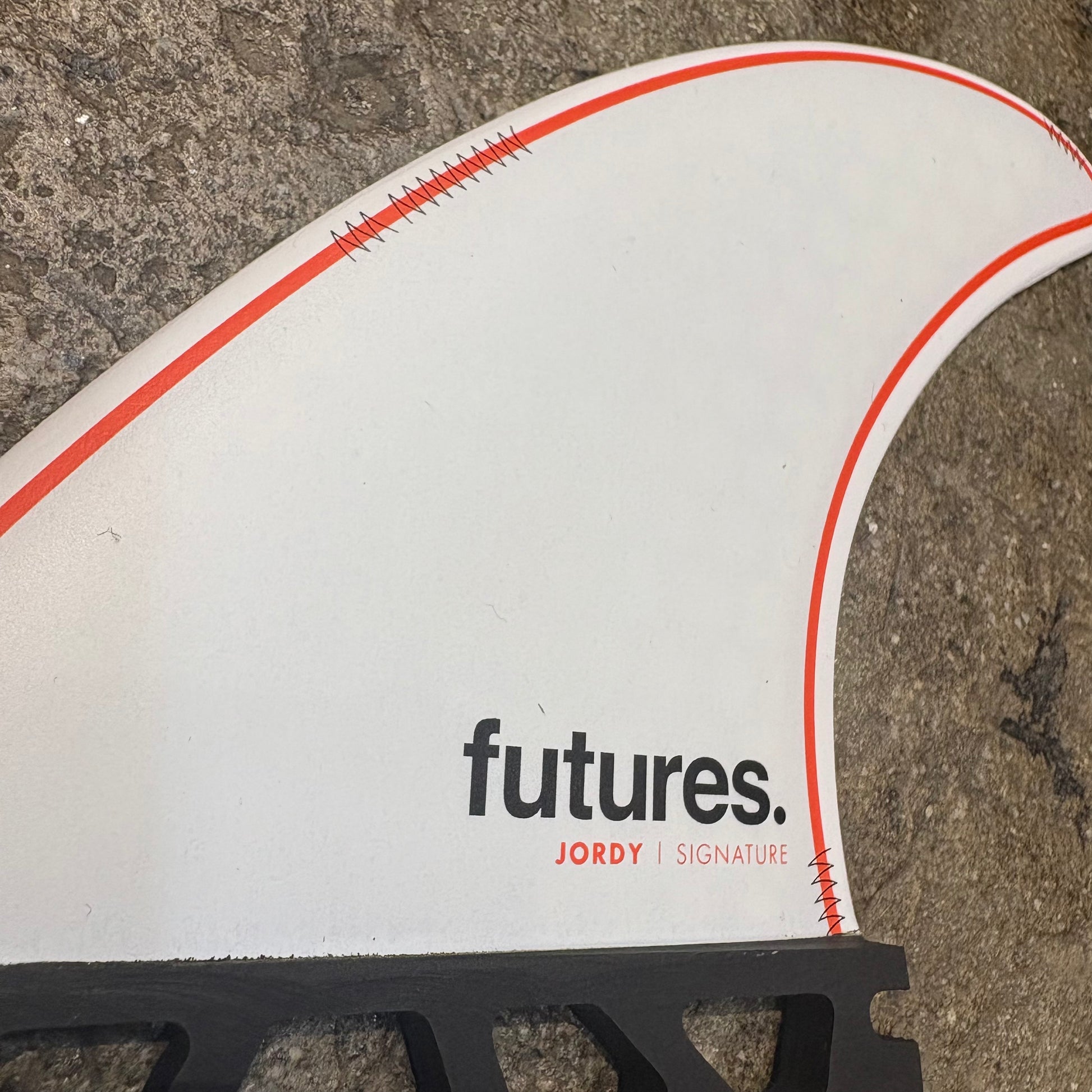 A single Jordy Smith Signature fin with 'futures.' branding,  in a white colour way with red details on a concrete surface