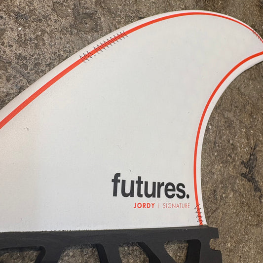 A single Jordy Smith Signature fin with 'futures.' branding,  in a white colour way with red details on a concrete surface