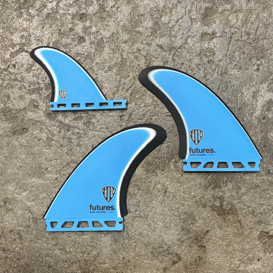 A set of Three blue Futures Mark Richards Twin+1 surfboard fins with on a concrete surface