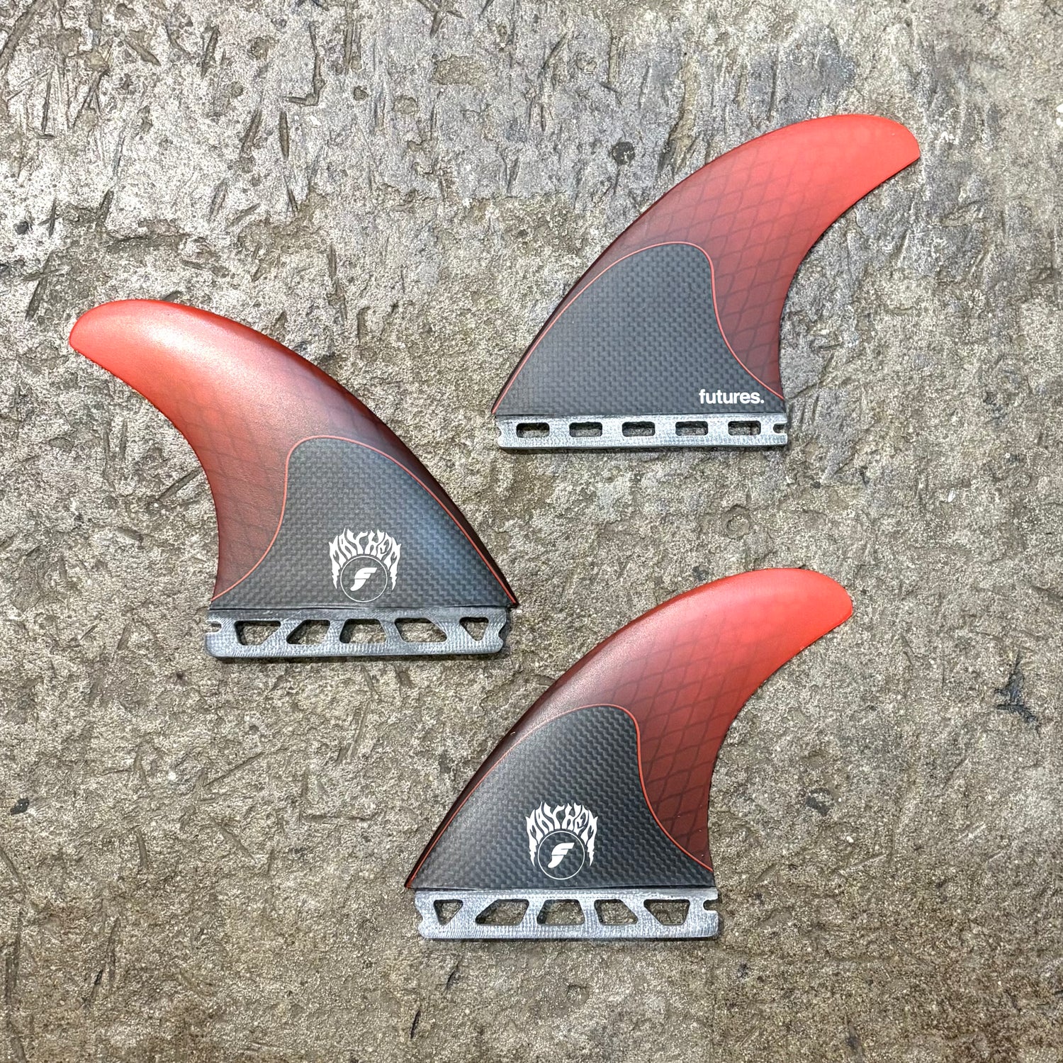 Three Futures Mayhem 3.0 Large red and black surfboard fins on a textured surface