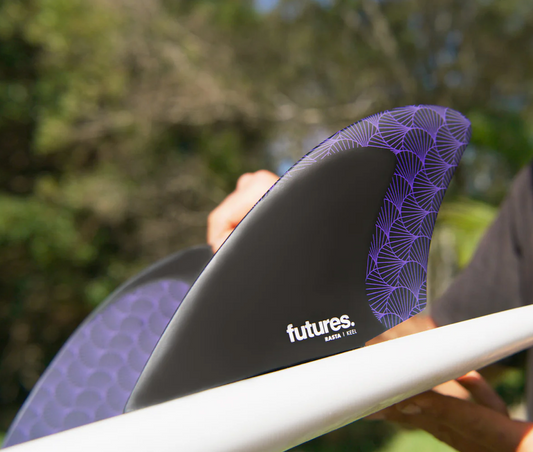 A pair of Futures Rasta Keels surfboard fins in a surfboard, with a blurry outdoor background.