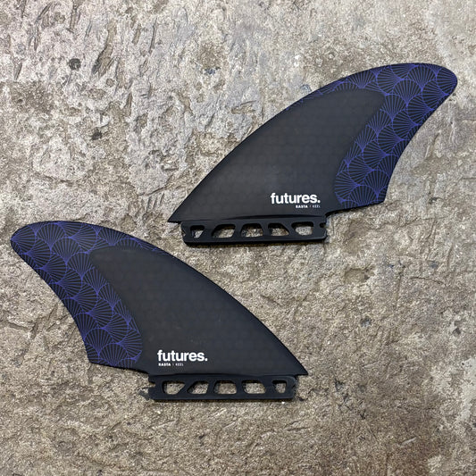 A pair of futures Rasta Keel surfboard fins with a black base and purple geometric pattern on a textured background.