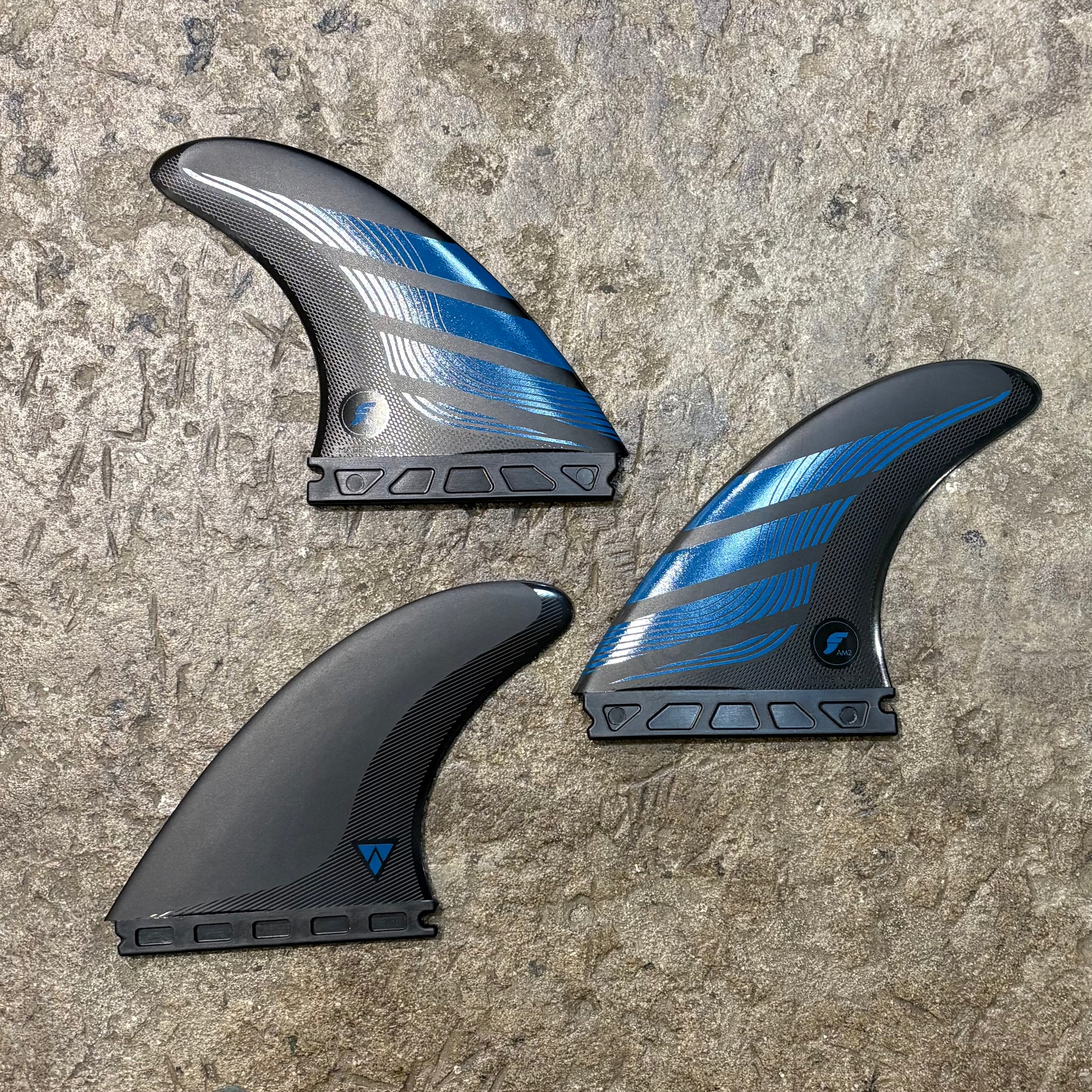 Three futures surfboard fins with blue and black design on a textured surface