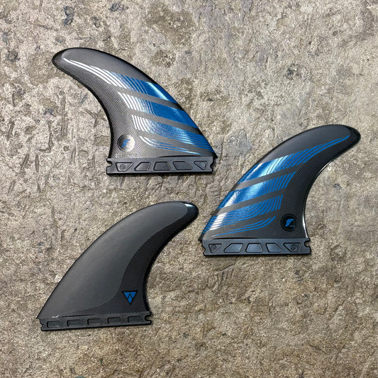 Three futures surfboard fins with blue and black design on a textured surface