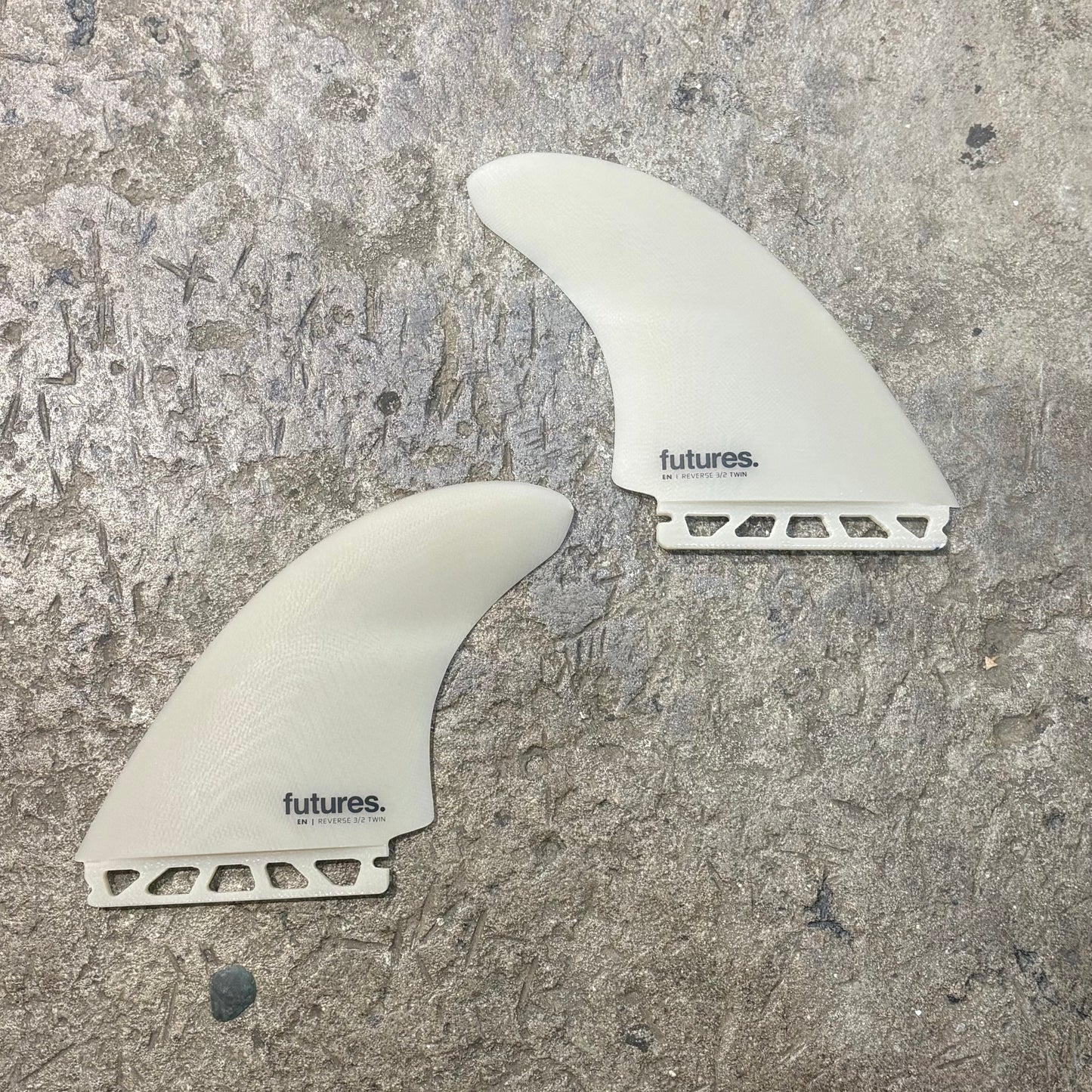 Two white FUTURES surfboard fins with 'futures' branding on a textured gray surface.