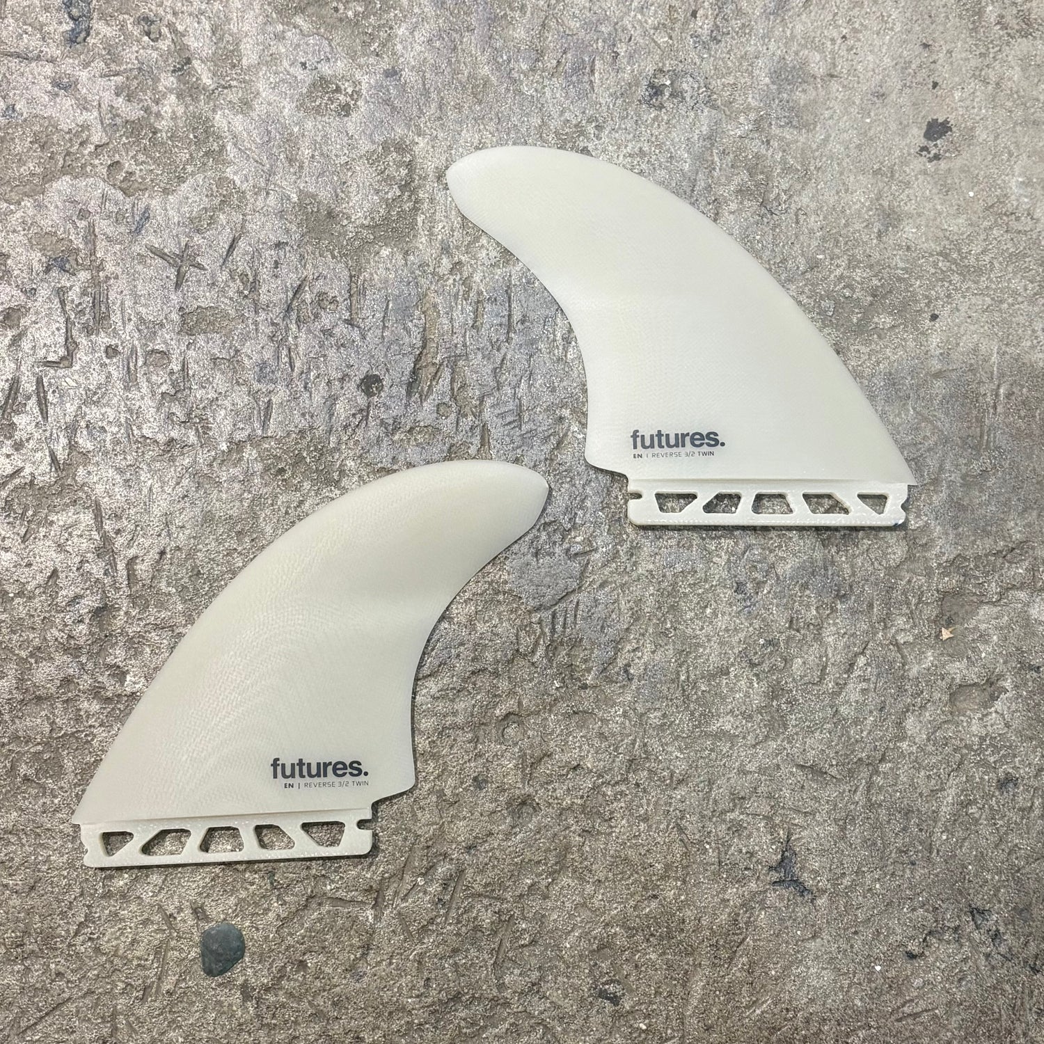 Two white FUTURES surfboard fins with 'futures' branding on a textured gray surface.