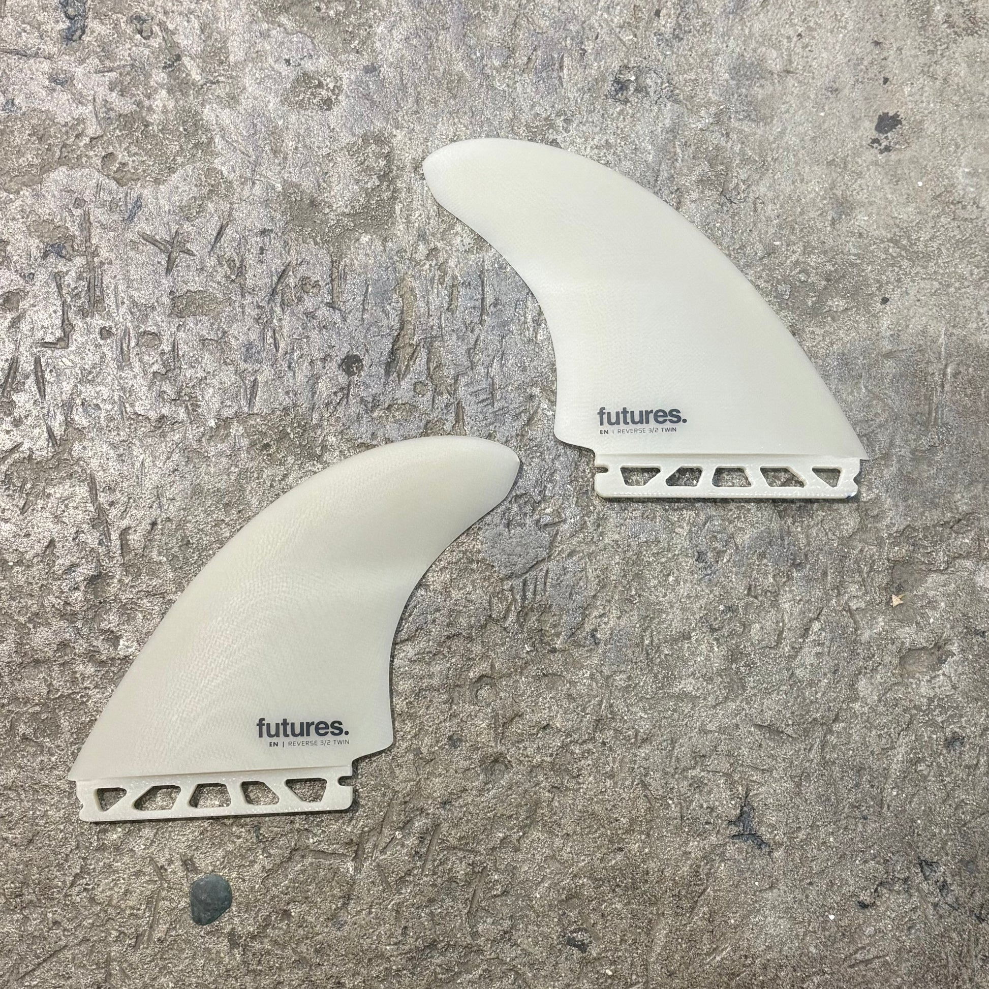 Two white FUTURES surfboard fins with 'futures' branding on a textured gray surface.