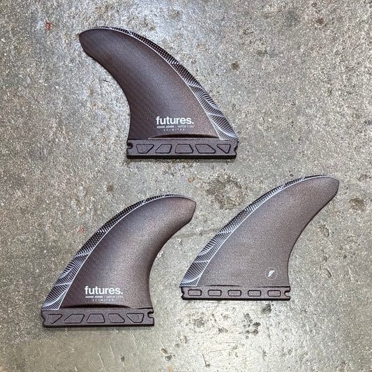 Three John John Florence surfboard fins with 'futures' branding on a concrete surface