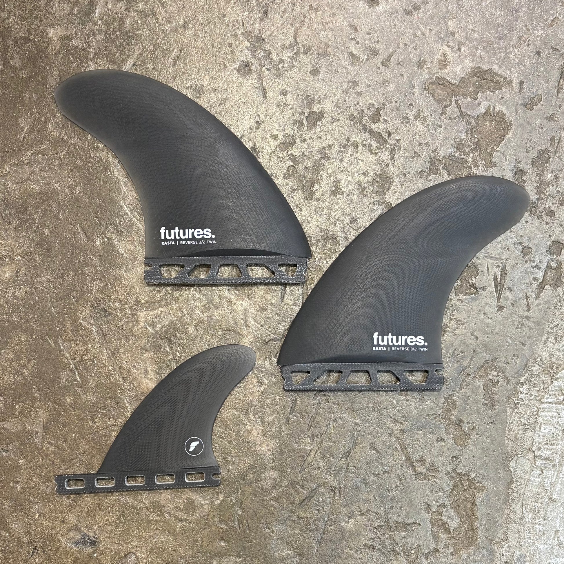 Three black surfboard fins with 'futures' branding on a textured surface.