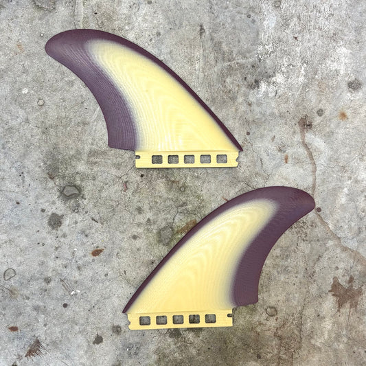 Two purple and yellow surfboard fins on a concrete surface