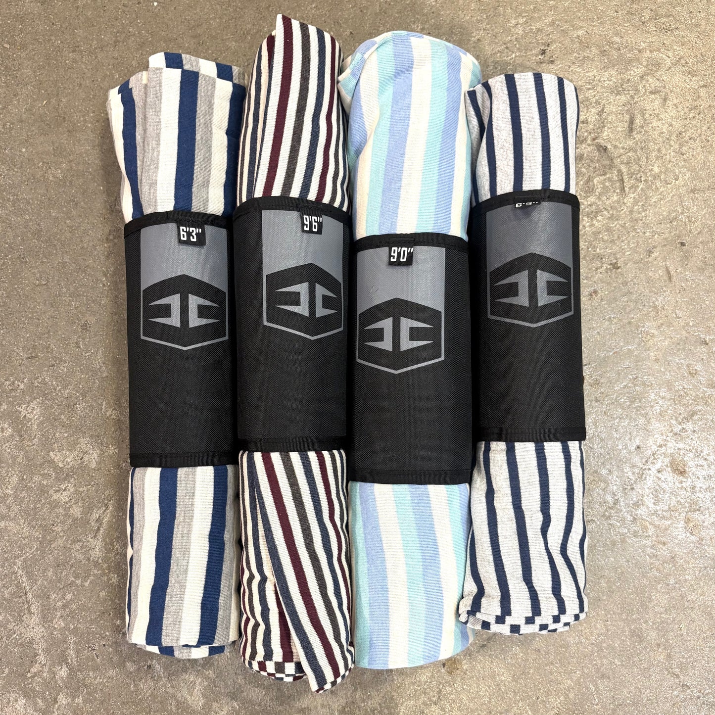 Four Hurricane folded surfboard socks with striped patterns and branded labels on a textured surface