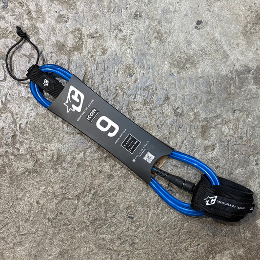 A blue and black Creatures of Leisure ICON 9 surf leash with a swivel bearing and a label detailing the product specifications placed on a textured ground.