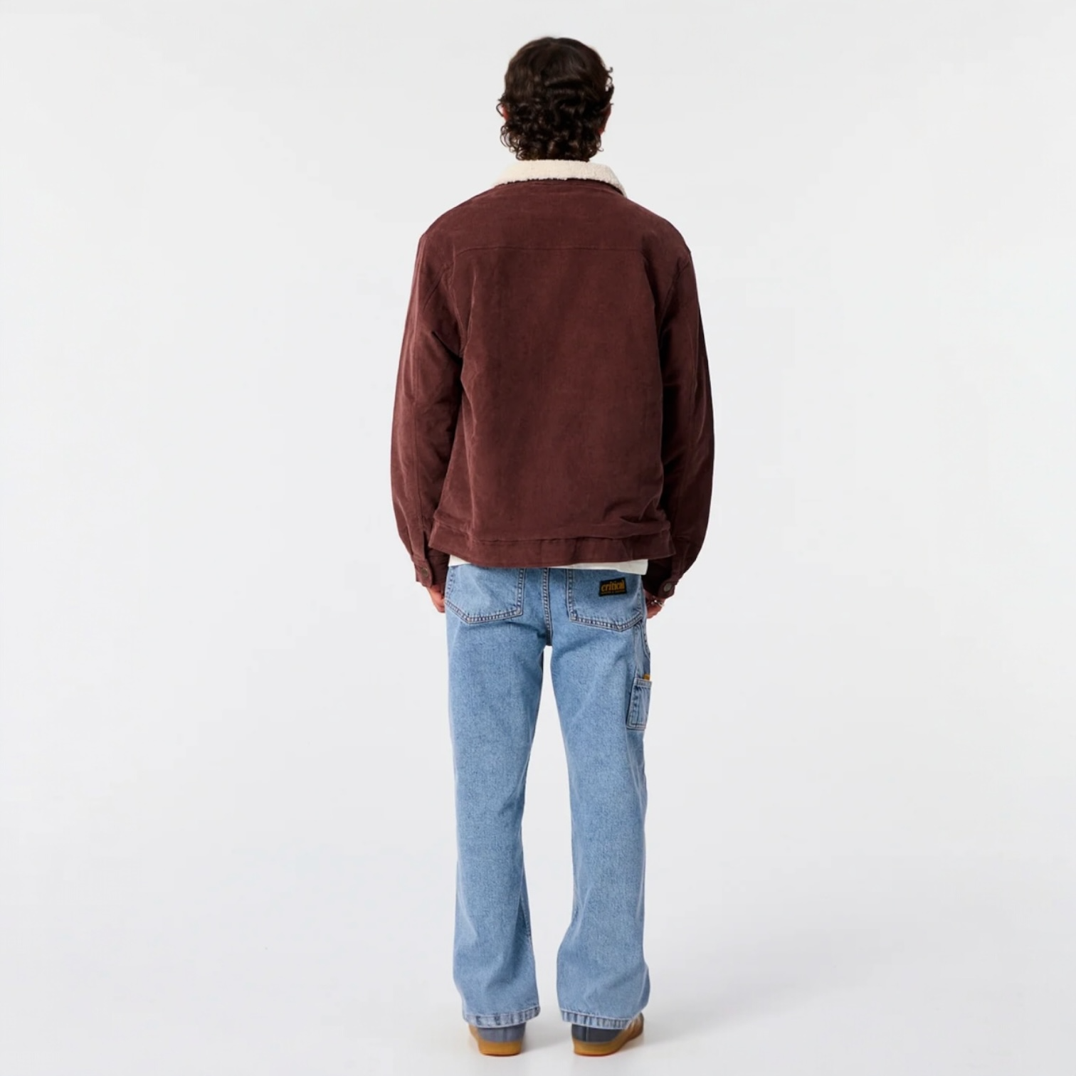 Person wearing a brown jacket and blue jeans on a white background