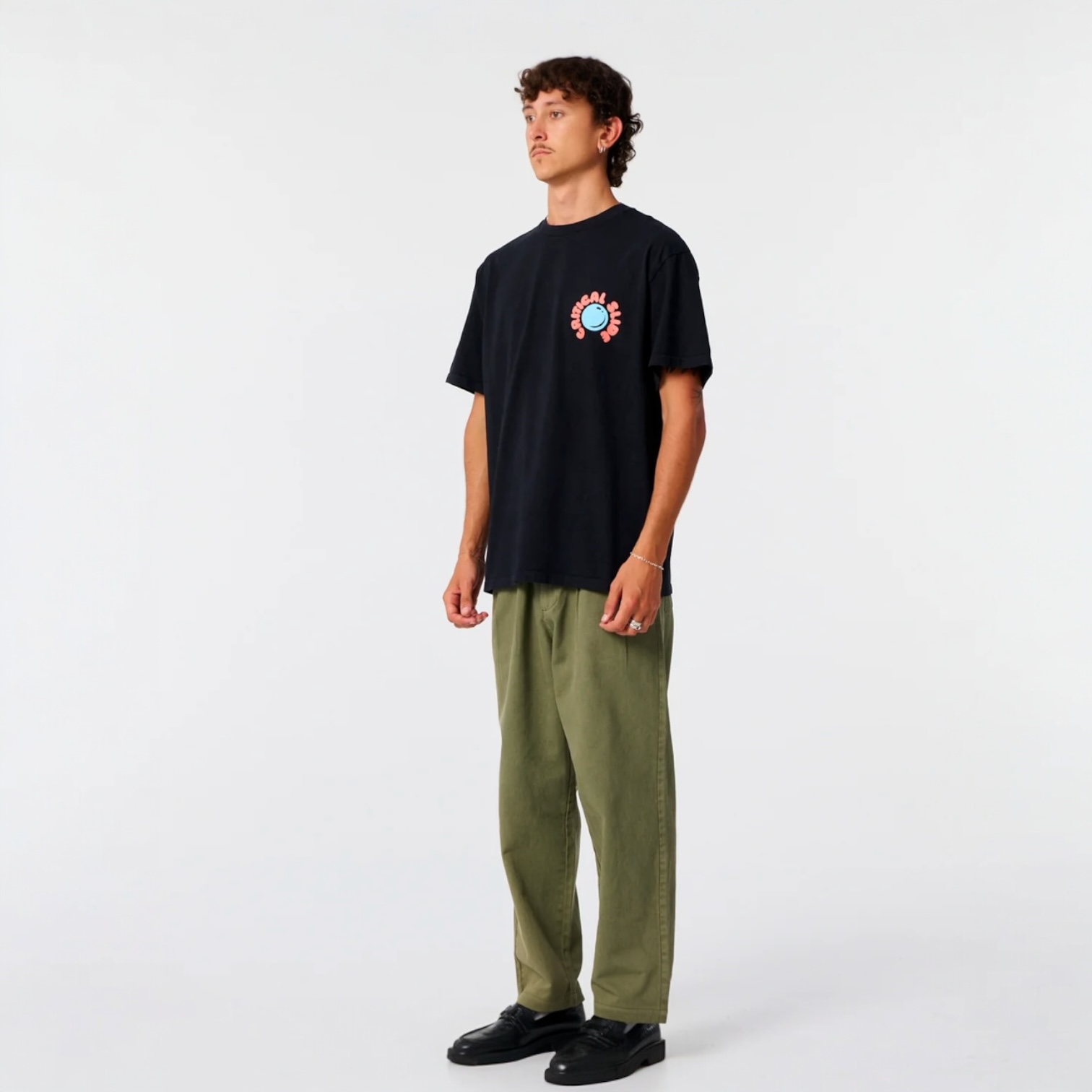 Person wearing a black t-shirt with a colorful graphic and green pants on a white background