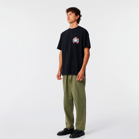 Person wearing a black t-shirt with a colorful graphic and green pants on a white background